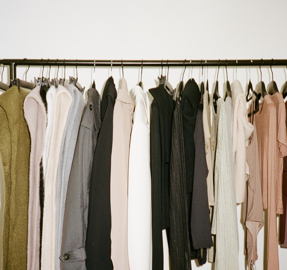 A rack of coats, knitwear and dresses in muted tones against a white wall