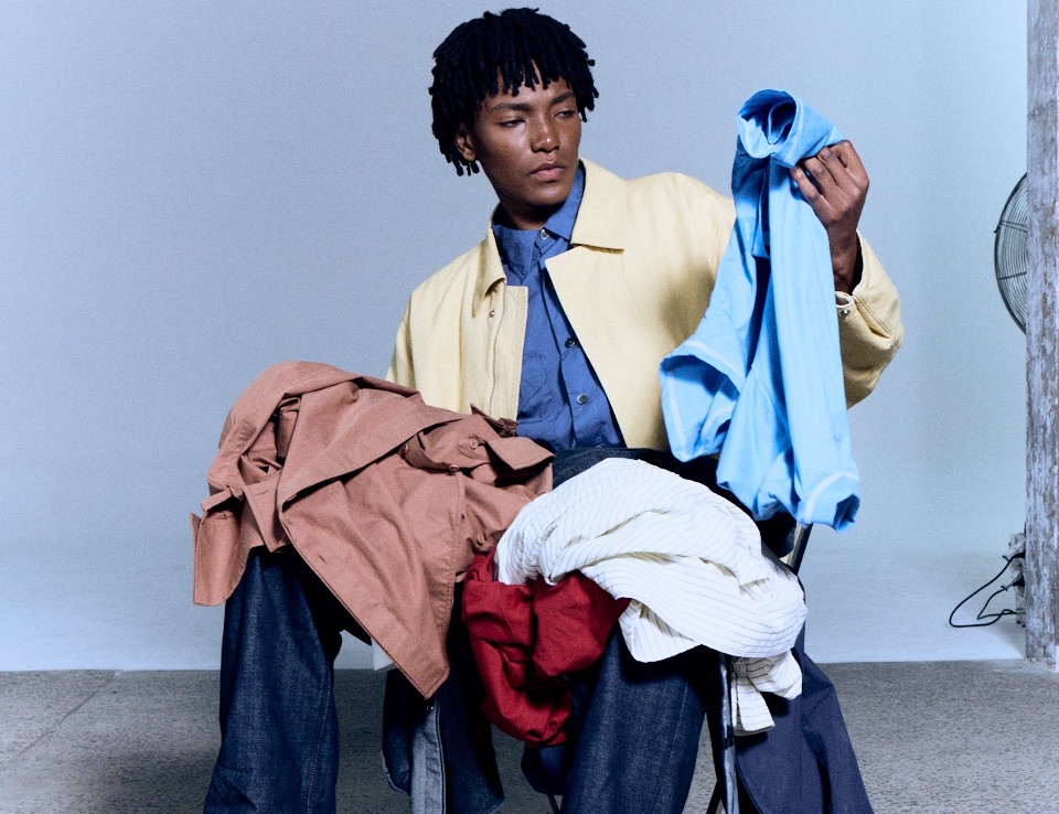 A man in a yellow jacket sorting a lap full of clothes he no longer wears