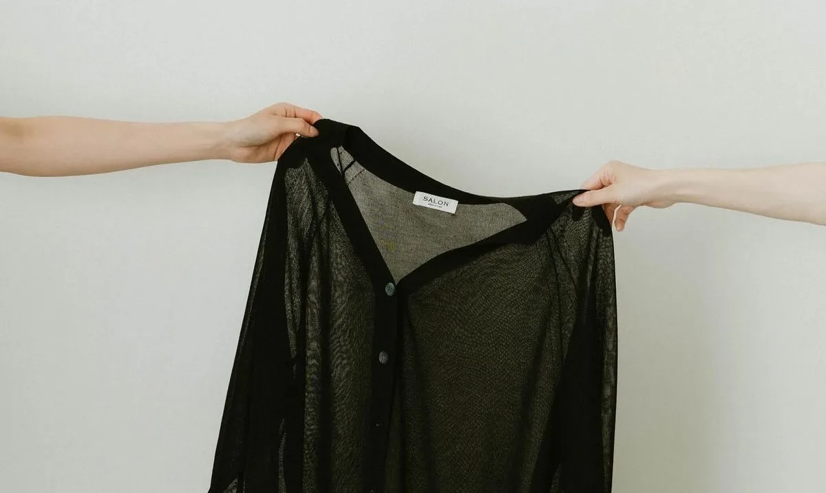 Two pairs of hands holding a black cardigan out between them