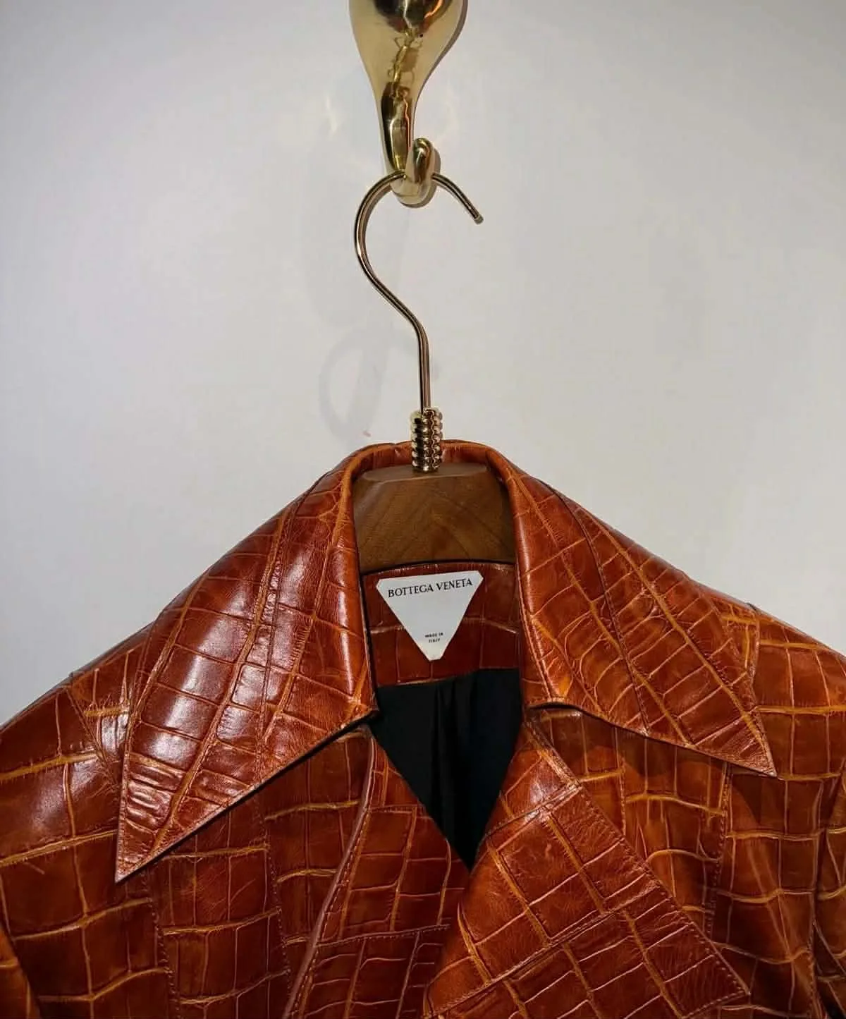 A tan crocodile-embossed leather jacket on a wooden hanger